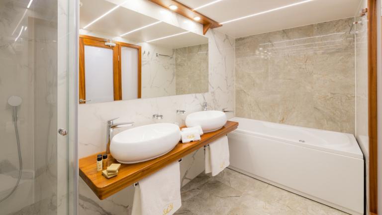 A noble bathroom made of light marble with a bathtub and two designer wash bowls.